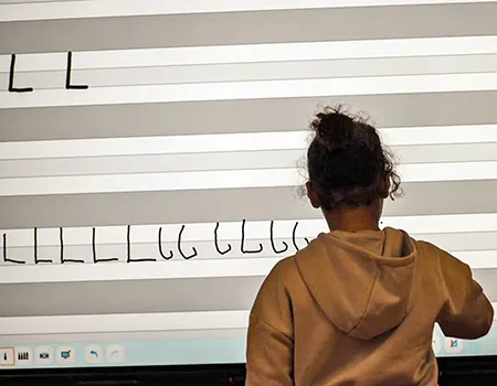 Kind schreibt den Buchstaben L an die Tafel