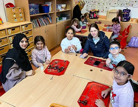 Eltern und Kinder sitzen am Schultisch und basteln Kastanienmännchen